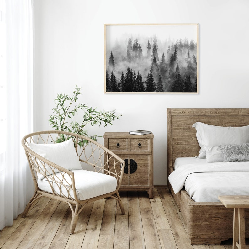 May include: Black and white photograph of a foggy forest scene. The image is framed and hanging on a white wall above a wooden bed and nightstand.