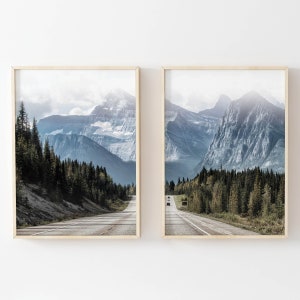 May include: Two framed prints of a scenic mountain road with a view of snow-capped mountains in the background. The road is lined with trees and the sky is a light blue with white clouds.
