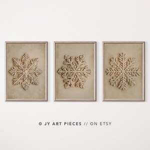 May include: Three framed wall art pieces featuring a beige background with a raised, white snowflake design in each frame.