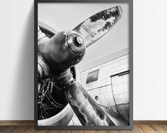 May include: Black and white photograph of a vintage airplane propeller. The propeller is made of metal and has a weathered look. The photo is taken from a close-up perspective, showing the details of the propeller blades and the engine.