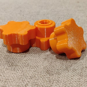 Może przedstawiać: Trzy pomarańczowe plastikowe gałki w kształcie gwiazdy z gwintowanym otworem w środku.