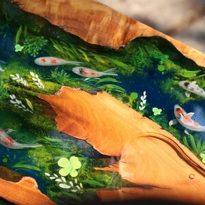 May include: A wooden artwork depicting a river scene with koi carp. The river is painted in blue and green tones, with white, orange, and black koi. The wood has a natural, warm brown colour.