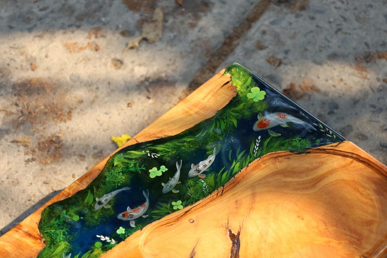 May include: Wooden serving tray with a river design. The tray features a clear resin river with koi fish, green plants, and clover accents. The tray's wooden surface has a natural wood grain.