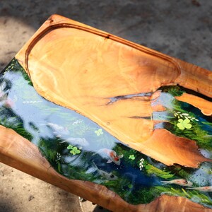 May include: Wooden serving tray with a river design. The tray has a light brown wooden border and a central river scene with koi carp, green plants, and blue water. The river is made of resin.