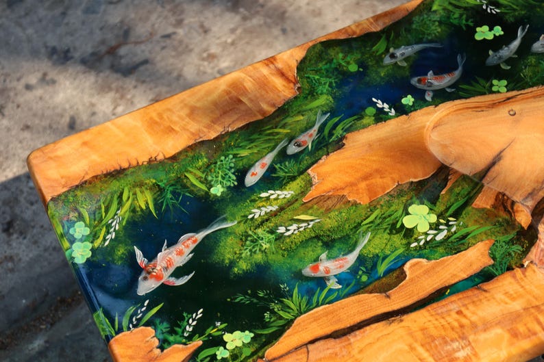 May include: A wooden table with a river scene. The table features a clear resin river with koi carp swimming among green plants. The wood has a natural, light brown colour, and the resin river is a deep blue.