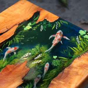 May include: Wooden table with a koi pond design. The table has a natural wood border and a central resin panel showing koi fish swimming among aquatic plants. The fish are white, orange, and black, with green and blue accents.