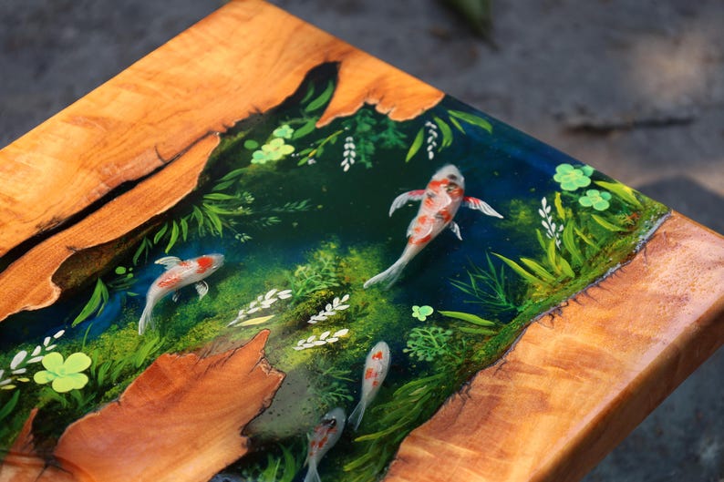 May include: Wooden table with a koi pond design. The table has a natural wood border and a central resin panel showing koi fish swimming among aquatic plants. The fish are white, orange, and black, with green and blue accents.