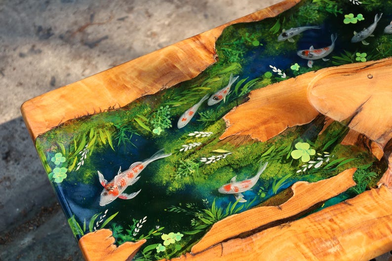 May include: A handcrafted wooden table with a river design. The river features a blue epoxy resin with koi carp and green plants. The table's edges are natural wood, showcasing the grain and texture. A unique piece for home decor.