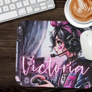 May include: A pink and purple gaming mouse pad with a cartoon illustration of a girl wearing headphones and holding a video game controller. The girl's name, "Victoria", is written in pink neon letters across the bottom of the mouse pad.