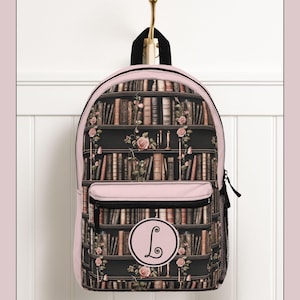Può includere: Uno zaino rosa e nero con un design a libreria, rose e candele. Lo zaino ha una parte superiore rosa, una tasca frontale e un emblema circolare con la lettera "L". La borsa è appesa a un gancio dorato.