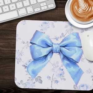 May include: A white mouse pad with a light blue bow and a floral pattern. The flowers are white with a light blue center.