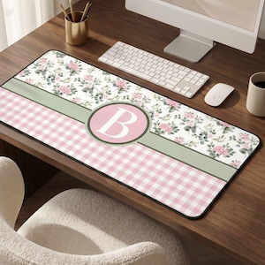 May include: A rectangular desk mat featuring a floral and gingham pattern in pink, white, and green. The mat has a large pink circle with the letter "B" in the center. The mat is designed to protect the desk surface.