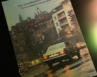 May include: A vintage advertisement for a car with the text "Het Anti-Blokkeer-Systeem. Een computer remt mee." and a Mercedes-Benz logo. The image shows a silver car driving on a wet street in a city setting.