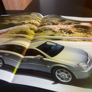 Op de afbeelding: Een zilvergrijze stationwagen rijdt op een kronkelende weg. De auto heeft een zwart interieur en een zwarte grille. De auto rijdt op een weg met groen gras en bomen aan beide kanten.