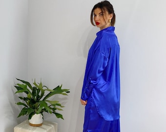 Puede incluir: Una mujer con una camisa de satén azul brillante y pantalones a juego. La camisa tiene cuello y mangas largas. Los pantalones son holgados y tienen una pierna recta.