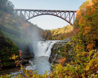 Peut inclure: Un pont en acier rouge en arc de cercle au-dessus d'une cascade dans une forêt. Les arbres sont dans leurs couleurs d'automne, avec des nuances de rouge, d'orange et de jaune. La cascade coule sur des rochers et crée une brume.