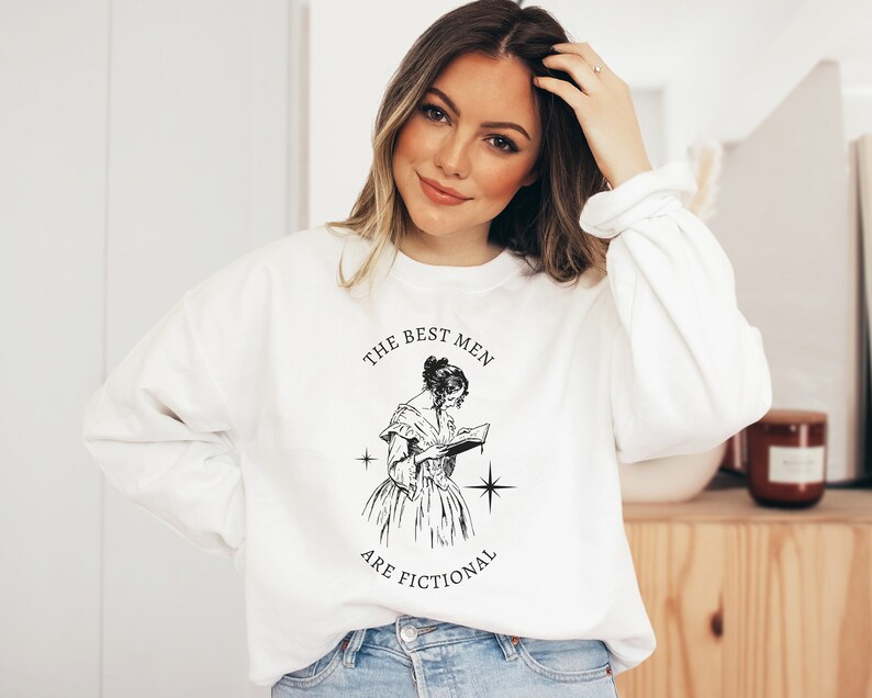 May include: White sweatshirt with a black graphic print of a woman reading a book. The text on the graphic reads "The Best Men Are Fictional".