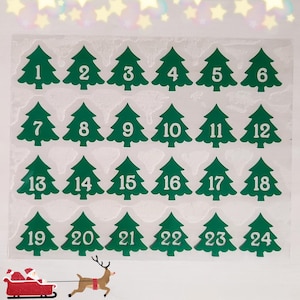 Könnte beinhalten: Ein Bogen mit grünen Weihnachtsbaum-Aufklebern mit den Nummern 1 bis 24. Jeder Baum hat eine weiße Nummer in der Mitte. Eine Grafik von Weihnachtsmann und Rentierschlitten befindet sich in der unteren linken Ecke. Der Hintergrund ist weiß.