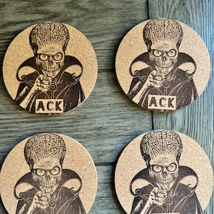 May include: Set of four round cork coasters featuring a black and white illustration of a character from the movie "Mars Attacks!" with the text "ACK" printed on each coaster.