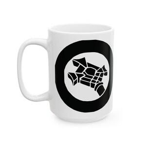 Puede incluir: Taza de cerámica blanca con un diseño gráfico negro. El diseño presenta un círculo negro con un interior blanco, que contiene una forma geométrica estilizada. La taza tiene un asa grande y es adecuada para bebidas frías o calientes.