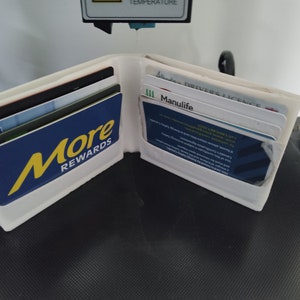 Puede incluir: Una cartera de plástico blanca con varias tarjetas en su interior. La cartera está abierta y las tarjetas son visibles. Las tarjetas incluyen una tarjeta "More Rewards", una tarjeta "Manulife" y una "Licencia de conducir".