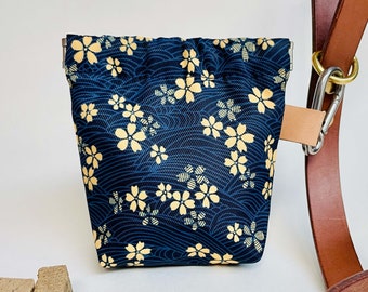 Op de afbeelding: Een blauwe en gele trekkoordtas met een bloemenpatroon. De tas is bevestigd aan een bruine leren riem met een metalen clip.