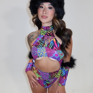 May include: A woman wearing a colorful, animal print bodysuit with a black fur-trimmed hat. The bodysuit has a cut-out design and a high neckline.