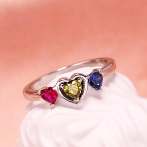 May include: A silver ring with three heart-shaped gemstones. The gemstones are red, yellow, and blue.