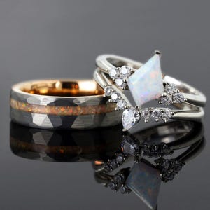 May include: Two rings, one with a hammered grey band and a gold interior, the other with a white opal and diamond accents. The opal ring has a geometric shape and is paired with a diamond-studded band. The rings are set against a dark background.