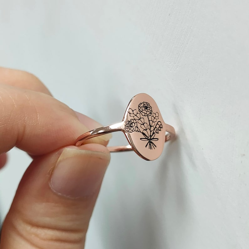 May include: A rose gold ring with an oval-shaped band featuring an engraved floral design.