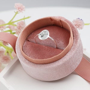 May include: A silver ring with a floral design sits in a pink velvet ring box.