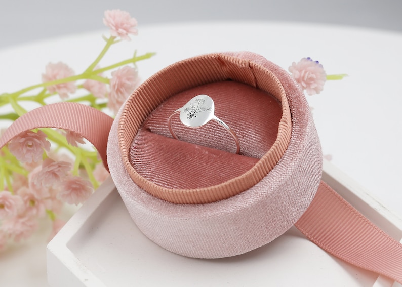 May include: A silver ring with a floral design sits in a pink velvet ring box.