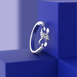 May include: A silver ring with a delicate design featuring two intertwined hearts and three small diamonds. The ring is displayed on a blue background.