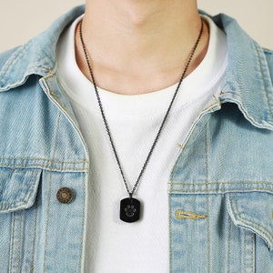 May include: A black chain necklace with a black rectangular pendant featuring a paw print design.