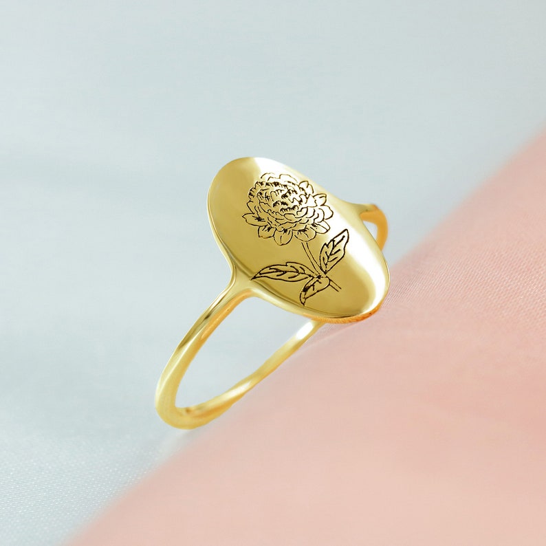 May include: A gold ring with an oval-shaped design featuring a delicate engraved flower.