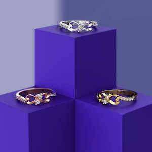 May include: Three infinity rings with diamonds on a purple background. The rings are in silver, rose gold, and gold.
