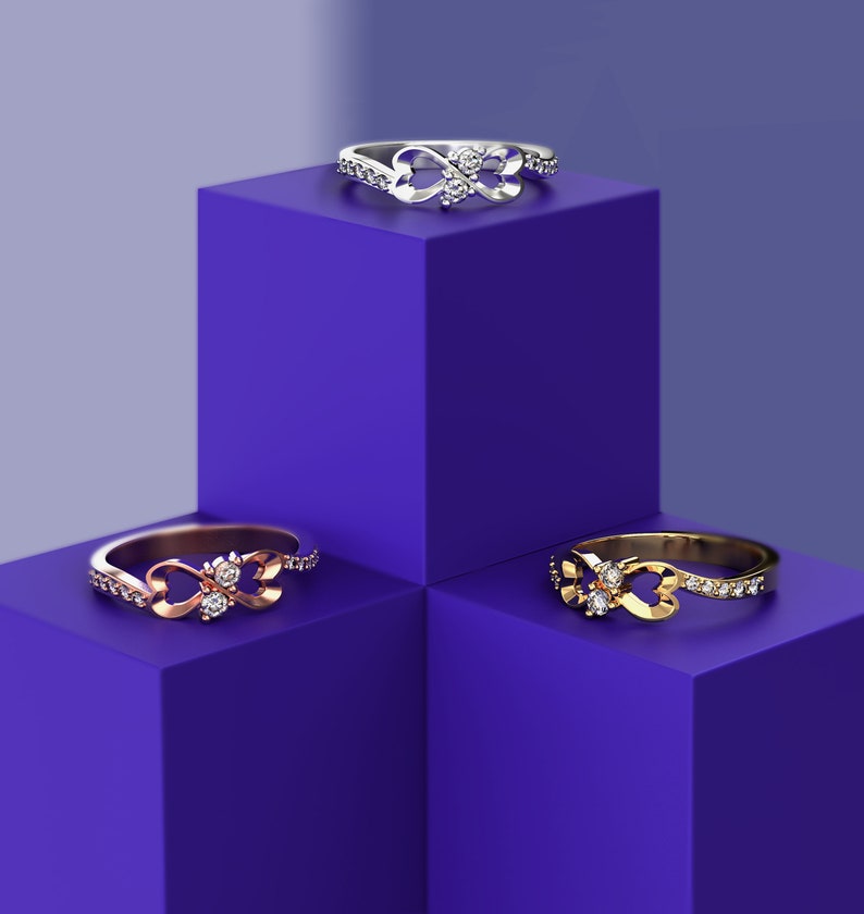 May include: Three infinity rings with diamonds on a purple background. The rings are in silver, rose gold, and gold.