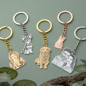 May include: A selection of personalised keyrings with engraved portraits and pet designs. The keyrings have various metal finishes, including silver, gold, and rose gold. The designs include a dog, a cat, a couple, and a portrait of a person.
