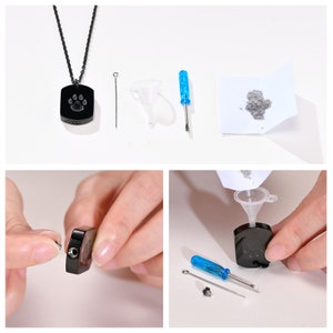 May include: A black necklace with a square pendant featuring a paw print. The pendant has a small screw on the side. The image also shows a small funnel, a screwdriver, and a small container of gray powder.