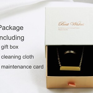 May include: A gold necklace with a bar pendant and a ring inside a white gift box with a gold ribbon. The box has the text "Best Wishes" on the top and "Remember you are my girl forever. Happy every day." inside. The box also includes a cleaning cloth and a maintenance card.