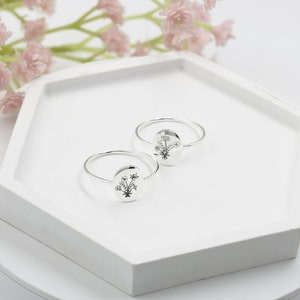 May include: Two silver rings with a floral design on the front. The rings are on a white hexagonal display stand.