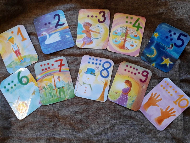 May include: Ten colorful cards with illustrations and braille dots representing the numbers 1 through 10. The cards are arranged in a semi-circle on a brown fabric surface.