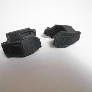 Puede incluir: Dos objetos negros impresos en 3D, posiblemente componentes de un artículo más grande, se muestran sobre un fondo blanco. Los objetos tienen un diseño geométrico con una superficie texturizada, lo que sugiere que fueron creados utilizando técnicas de fabricación aditiva.