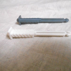 Może przedstawiać: Dwa plastikowe, cylindryczne przedmioty. Jeden jest biały, drugi ma stonowany szaro-niebieski kolor. Oba mają prostokątną gł&oacute;wkę z żebrowaną powierzchnią i cylindryczny korpus. Końce mają mały, zaokrąglony guzik.