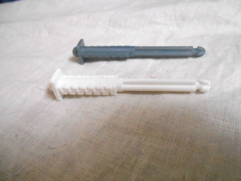 Może przedstawiać: Dwa plastikowe, cylindryczne przedmioty. Jeden jest biały, drugi ma stonowany szaro-niebieski kolor. Oba mają prostokątną gł&oacute;wkę z żebrowaną powierzchnią i cylindryczny korpus. Końce mają mały, zaokrąglony guzik.