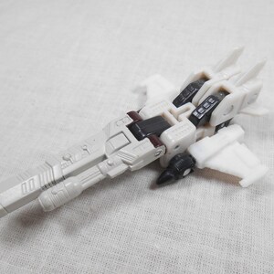 May include: A white and gray toy airplane with black and maroon accents. The toy has a long, cylindrical body with wings and a detailed design. The toy is made of plastic and appears to be a model or collectible item.