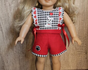 May include: A doll wearing a red and black gingham dress with a white dog applique and red ribbon ties. The doll has blonde hair and blue eyes and is wearing white shoes.
