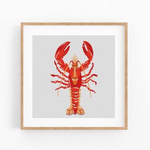 May include: A framed cross-stitch art piece featuring a detailed red and orange lobster design. The crustacean is centered against a light gray background, with a wooden frame. The lobster's claws are raised, and the artwork has a handmade aesthetic.