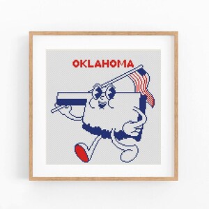 May include: A framed cross-stitch art piece featuring a cartoon character representing the state of Oklahoma. The character is a white shape with a blue outline, holding a flag and wearing sunglasses. The word "OKLAHOMA" is in red letters above.