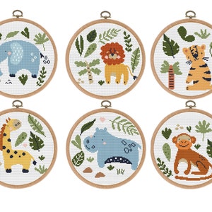 Può includere: Sei cerchi da ricamo con diversi disegni di animali della giungla. Gli animali includono un elefante, un leone, una tigre, una giraffa, un ippopotamo e una scimmia. Ogni cerchio ha uno sfondo bianco con foglie verdi e cerchi in legno marrone.